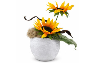 Twee gele kunstzonnebloemen met groen blad, vlas en gebogen bruine decoratie in een ronde lichtgrijze pot met betonlook