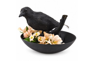 Oiseau décoratif noir perché sur du bois parmi des fleurs couleur saumon dans une coupe ronde noire